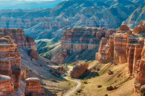 Beeindruckende Schluchten und Berge prägen die Kasachstan Landschaft. Ein gewundener Weg führt durch das Tal, umgeben von roten Felsformationen und grünen Hängen.
