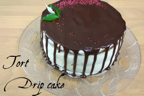 Pyszny tort drip cake z czekoladą spływającą po bokach, ozdobiony różową posypką i listkami.