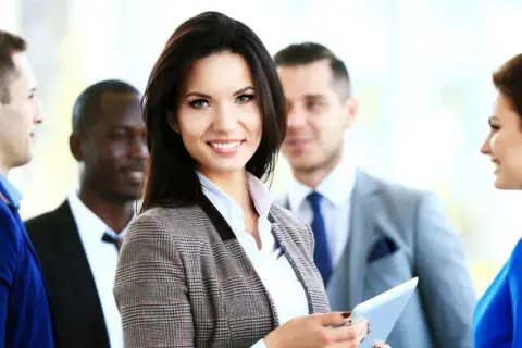 Team di professionisti sorridenti, con una donna in primo piano che tiene un tablet. Un esempio di chi partecipa a un corso RLS cos'è.