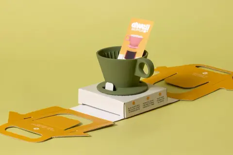 Minimalist packaging design trends 2024: a green coffee dripper with instructions on a yellow cardboard box.