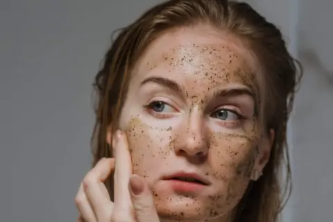 Una donna applica uno scrub viso, scoprendo i benefici di una pelle liscia e luminosa.