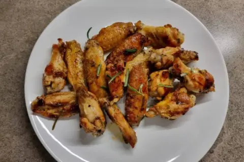 Alette di pollo in padella, dorate e succulente, guarnite con rosmarino fresco. Un piatto invitante pronto per essere gustato.
