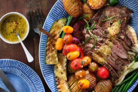 En saftig flankstek, perfekt för att grilla, serveras med grillade grönsaker som zucchini, tomater, potatis och gröna bönor. En härlig måltid!