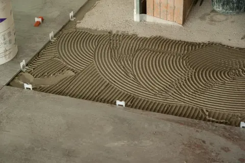 Pose de carrelage : la chape maigre attend les carreaux, avec des croisillons blancs et un lit de colle strié.