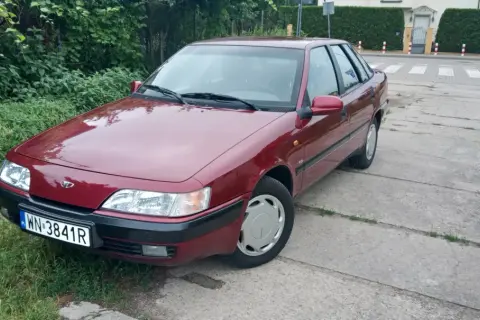 Czerwony Daewoo Espero z tablicą rejestracyjną WN-3841R zaparkowany przy zarośniętym poboczu i betonowej drodze.