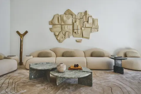 Salon moderne avec canapé beige, tables basses en marbre vert, sculpture murale abstraite et tapis aux motifs organiques. Un endroit parfait pour recevoir une lettre home.