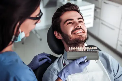 Dentystka dobiera odcień licówek kompozytowych dla uśmiechniętego pacjenta.