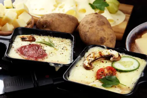 Schmelzender Raclette-Käse mit Salami und Pilzen, dazu Kartoffeln und ein Glas Wein. Perfekt für einen gemütlichen Abend.
