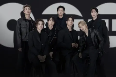 Die Mitglieder von BTS posieren in schicken schwarzen Outfits vor einem großen, stilisierten "GQ"-Logo.
