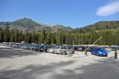 Parking pod Morskim Okiem, pełen samochodów, z górami i lasem w tle.