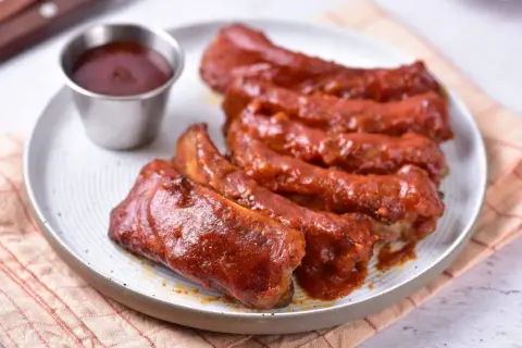 Soczyste żeberka w sosie BBQ, podane na talerzu z małą miseczką sosu. Idealne na letniego grilla.