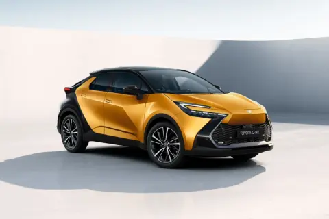 Nowy Toyota C-HR Hybrid w kolorze złotym, z czarnym dachem i felgami, prezentuje się nowocześnie na tle białej ściany.