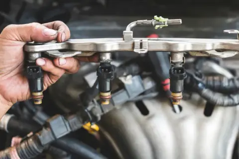 Mano sosteniendo un riel de inyectores de combustible, parte esencial del sistema de inyección directa de un motor.