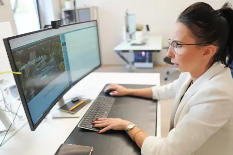 Kobieta w okularach pracuje przy komputerze, na ekranie której widoczna jest darmowa strona internetowa z ofertą konsultacji ślubnych.