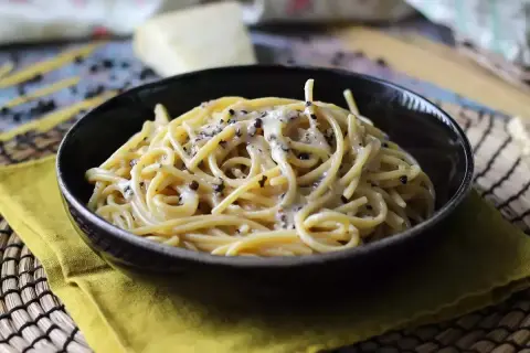 Miseczka spaghetti cacio e pepe, z kremowym sosem serowym i pieprzem, na żółtej serwetce.