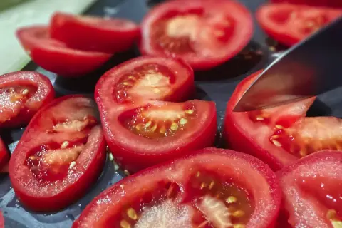 Pokrojone pomidory na desce. Potas na co pomaga? Wpływa na ciśnienie i pracę serca, a pomidory są jego dobrym źródłem.