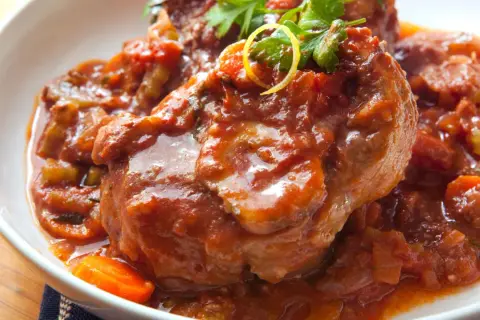 Herzhaftes Ossobuco Rezept in Tomatensoße mit Karotten und Petersilie, serviert in einer weißen Schüssel.