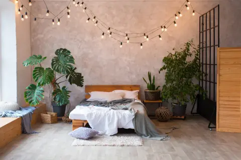 Przytulna sypialnia boho loft z łóżkiem, roślinami i girlandą świetlną.
