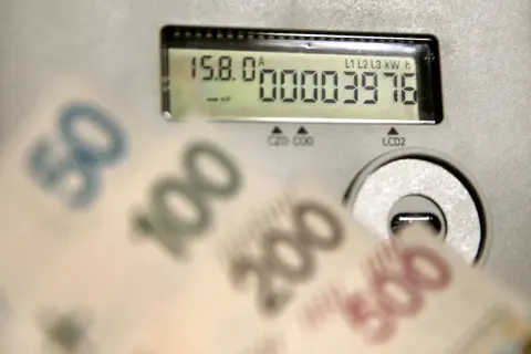 Liczniki energii PGE pokazują zużycie, a przed nimi banknoty 50, 100, 200, 500 zł. Opłata sieciowa PGE może być wysoka.