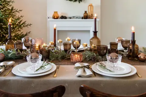 Une table de fête dressée avec une nappe intissé, des bougies, des verres ambrés et des décorations de Noël.