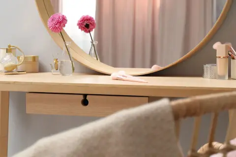Eleganckie krzesło do toaletki z rattanowym oparciem, obok drewnianego blatu z kosmetykami i kwiatami.