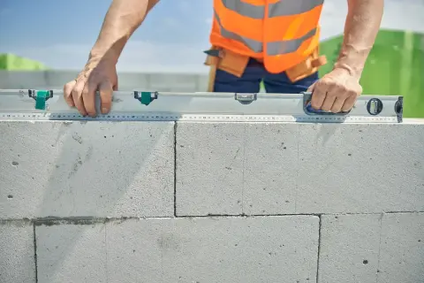 Budowniczy sprawdza poziom ścianki z bloczków. Dokładne wymierzenie ile suporexu na m2 jest kluczowe dla stabilności konstrukcji.