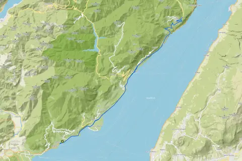 Il lungolago di Gardone Riviera si estende lungo il Lago di Garda, con montagne verdi che si affacciano sull'acqua.