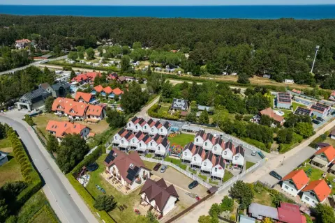 Widok z lotu ptaka na Dębki: domki z czerwonymi dachami, las i morze w tle.