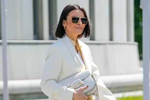 Elegancka kobieta po 50. w białej marynarce i okularach przeciwsłonecznych, z białą torebką. Stylowa moda po 50.