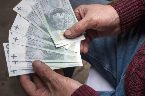 Ręce trzymające polskie banknoty. Zastanawiasz się, jaka emerytura przy zarobkach 7000 brutto?