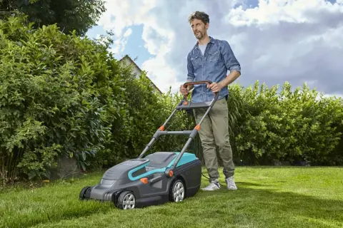 Mężczyzna z kosiarką elektryczną, która jest jedną z najlepszych kosiarek elektrycznych, dba o swój zielony trawnik.