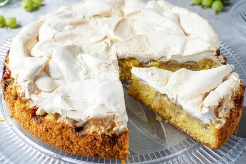 Ein köstlicher Stachelbeer Baiser Kuchen mit goldbraunem Boden und fluffiger Baiserhaube, ein Stück ist bereits angeschnitten.