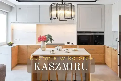 Elegancka kuchnia w kolorze kaszmiru z drewnianymi frontami i marmurowym tłem. Na wyspie bukiet kwiatów i zastawa.