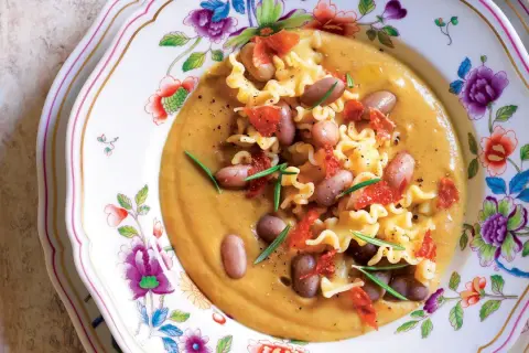 Pasta e Fagioli with ruffled pasta, beans, and crispy pancetta on a floral plate.