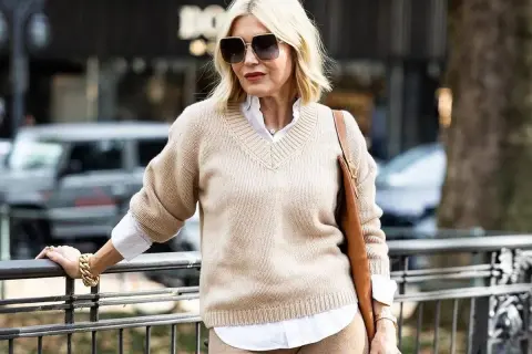 Eleganckie zestawy ubrań dla 50-latki: beżowy sweter, biała koszula i brązowa torebka. Stylowa kobieta w modnej stylizacji.