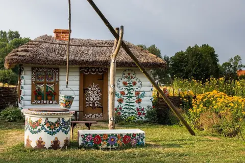 Tradycyjna chata z malowanymi kwiatami, studnia i kwitnące żółte kwiaty. Wygląda jak najpiękniejsza wieś w Polsce.