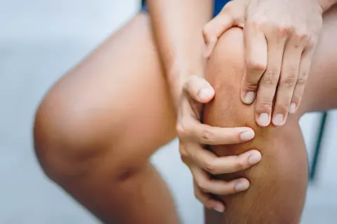 Hände umfassen ein schmerzendes Knie. Was tun bei Knieschmerzen?