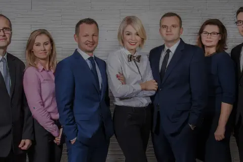 Grupa prawników w eleganckich strojach pozuje do zdjęcia na tle ściany z cegły.