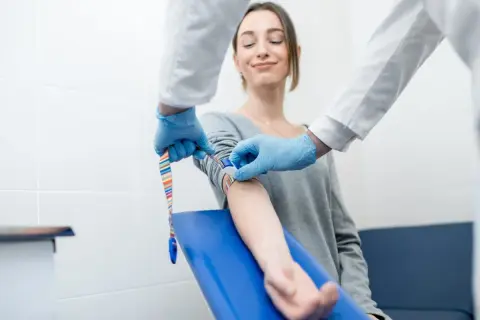 Pobieranie krwi do badania kreatyniny. Czy badanie kreatyniny robi się na czczo? Pacjentka uśmiecha się, gdy pielęgniarka pobiera krew.