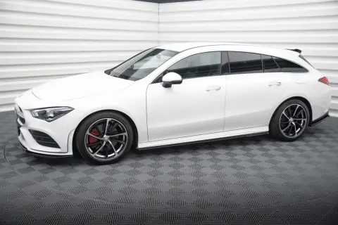 Biały Mercedes CLA shooting brake z czarnymi felgami i czerwonymi zaciskami hamulcowymi stoi na szarej, kratkowanej podłodze.