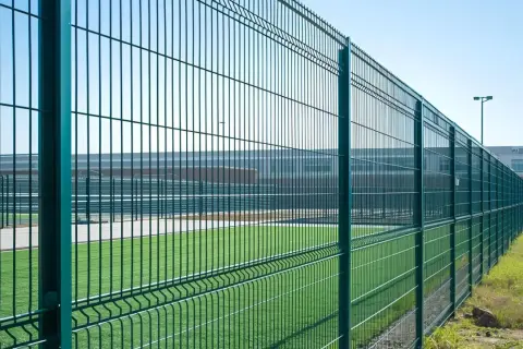 Zielona siatka ogrodzeniowa otacza boisko. Czy można ogrodzić działkę rolną podobnym płotem?