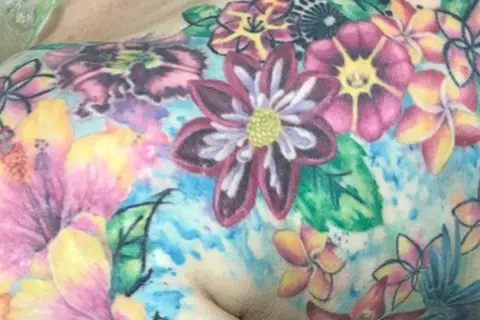 Buntes Blumen-Tattoo, das Lebensfreude nach einer Krebserkrankung symbolisiert. Hibiskus und andere tropische Blüten in leuchtenden Farben.