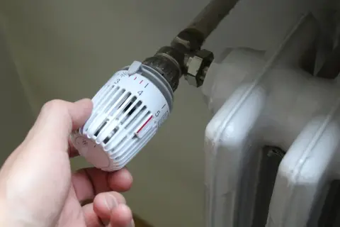 Mano che regola la manopola del termosifone, scegliendo tra senso orario o antiorario per la temperatura desiderata.