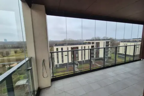 Zabudowa balkonu w bloku z widokiem na nowoczesne osiedle. Szklane panele tworzą przestronną, przeszkloną loggię.
