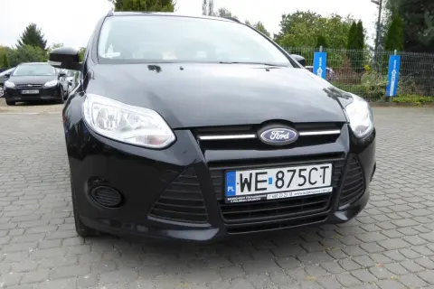 Czarny Ford Focus 2011 z tablicą WE 875CT zaparkowany na kostce brukowej.