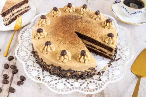 Eine köstliche Mokka Torte, verziert mit Kaffeebohnen und Schokostückchen, wartet auf Genießer. Daneben ein Stück Torte und eine Tasse Kaffee.