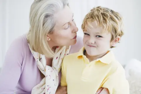 Una nonna bacia un bambino sorridente. Nonostante la tenerezza, i bambini non si baciano sempre, ma questo momento è speciale.