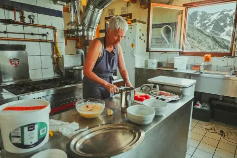 Une femme prépare des ingrédients dans une cuisine de montagne, un aperçu de son quotidien à travailler dans un refuge.