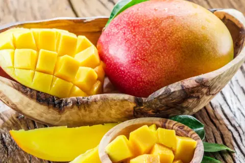 Dojrzałe mango w drewnianej misce, pokrojone w kostkę i plastry. Słodki owoc, który warto znać jego mango kcal.