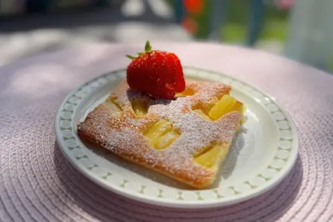 En bit saftig ananaskaka i långpanna, pudrad med florsocker och toppad med en färsk jordgubbe. Perfekt för en sommardag.